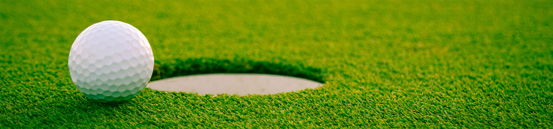 A golf ball near a hole on a green putting surface, showcasing the texture of the grass.