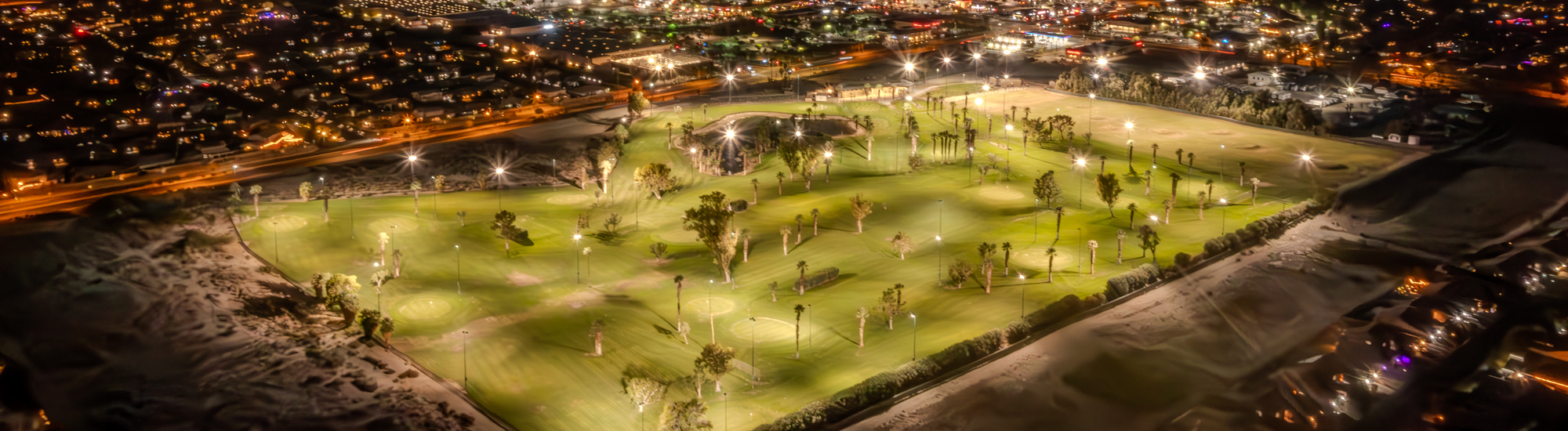 Aerial view of a well-lit golf course surrounded by city lights at night.