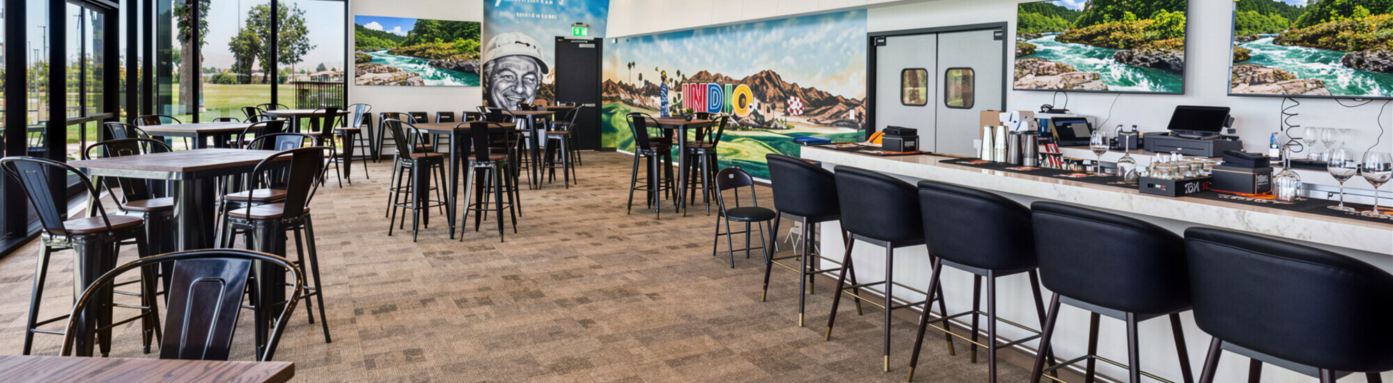 Modern dining area with high tables and chairs, featuring large windows and vibrant wall art.