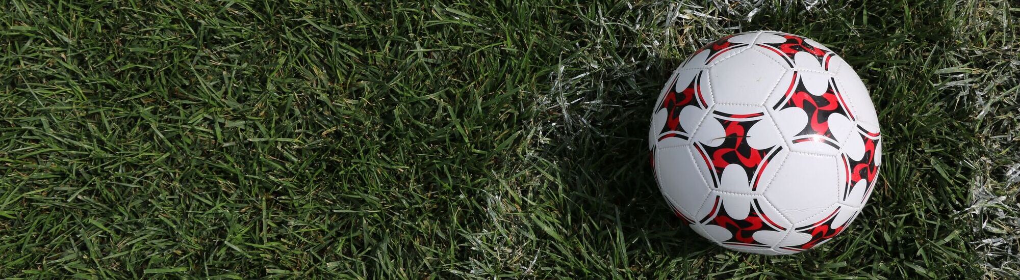 A footgolf ball with a distinctive red and black design resting on green grass.